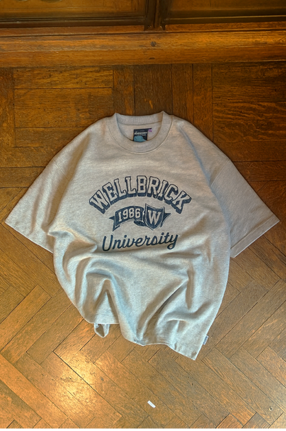 Gray t-shirt with 'Wellerick University' text on a wooden floor